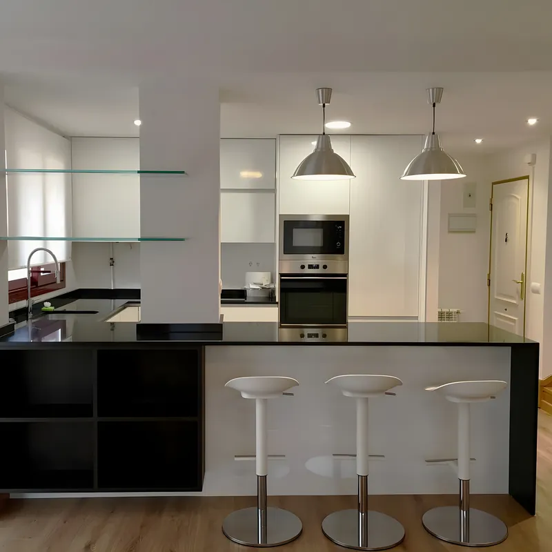 Cocina en blanco y negro con península, taburetes y lámparas colgantes