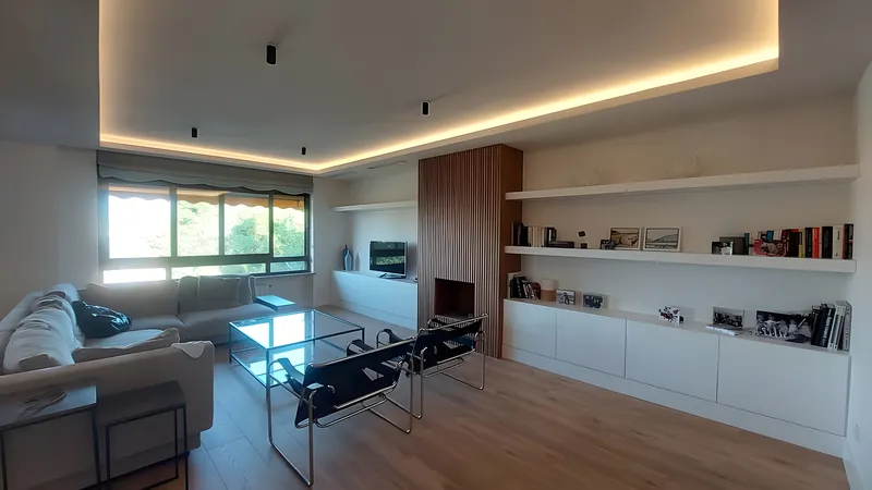 Salón reformado con luz indirecta en el techo, librería blanca y suelo de tarima